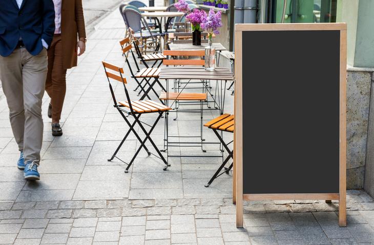 Blank menu blackboard on the street with cafe chairs and people passing by